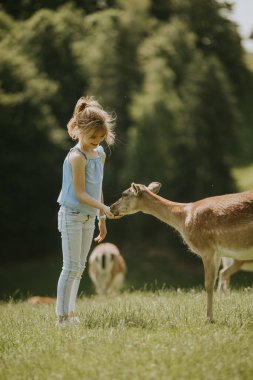 Cute little girl among reindeer herd on the sunny day