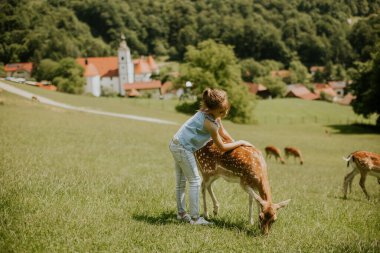 Cute little girl among reindeer herd on the sunny day