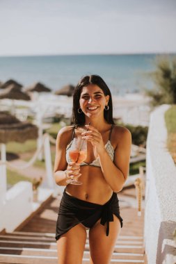 Gülümseyen genç kadın Bikini 'de kokteyl içerken tatilin tadını çıkarıyor.