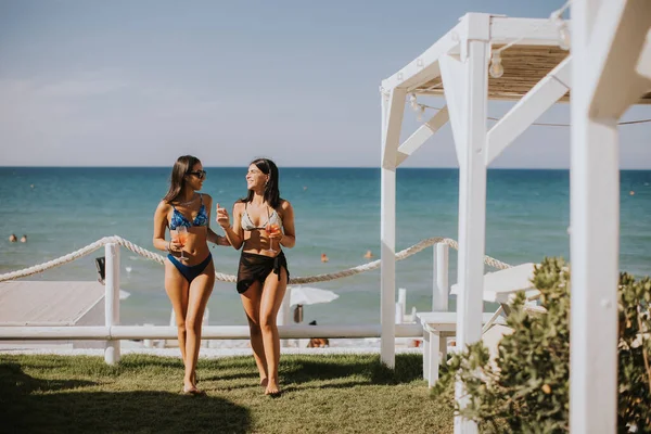 Duas Jovens Mulheres Sorridentes Biquíni Desfrutando Férias Praia Enquanto Bebem — Fotografia de Stock