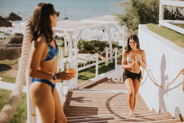 Dos Jóvenes Sonrientes Bikini Disfrutando Vacaciones Playa Mientras Beben Cóctel —  Fotos de Stock