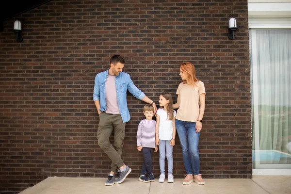 Family with a mother, father, son and daughter standing by the wall of a brick house