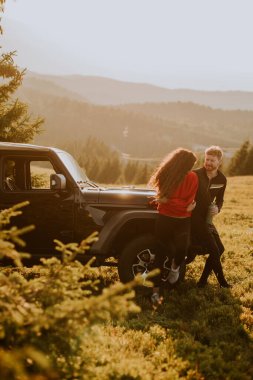 Handsome young couple relaxing by a terrain vehicle hood at countryside