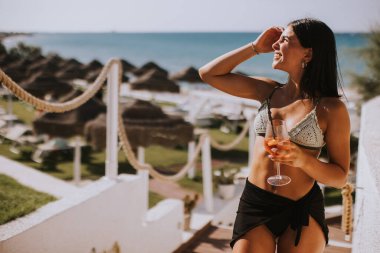 Gülümseyen genç kadın Bikini 'de kokteyl içerken tatilin tadını çıkarıyor.