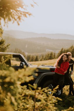 Handsome young couple relaxing by a terrain vehicle hood at countryside