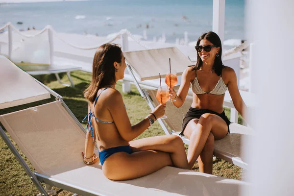 两个穿着比基尼 面带微笑的年轻女子一边喝酒一边在海滩度假 — 图库照片