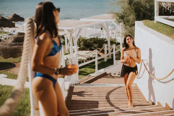 Dos Jóvenes Sonrientes Bikini Disfrutando Vacaciones Playa Mientras Beben Cóctel — Foto de Stock