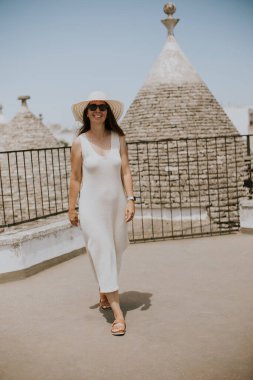 Güneşli bir günde beyaz elbiseli ve şapkalı genç bir kadın Alberobello, İtalya 'da turist ziyareti sırasında