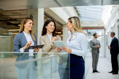 Dijital tabletleri olan üç genç iş kadını ofis koridorunda iş fikirlerini tartışıyor.