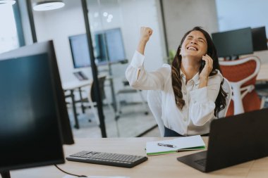 Modern ofiste dizüstü bilgisayarla çalışırken cep telefonu kullanan genç ve güzel bir iş kadını.