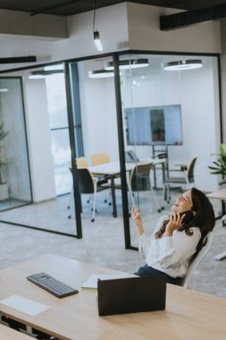 Modern ofiste dizüstü bilgisayarla çalışırken cep telefonu kullanan genç ve güzel bir iş kadını.