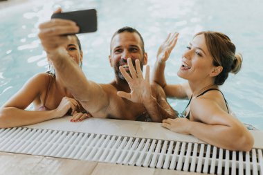 Yakışıklı gençler kapalı havuzda rahatlıyor ve cep telefonuyla selfie çekiyor.