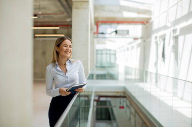 Modern ofis duvarında duran defterli genç bir iş kadını.