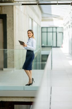 Modern ofis duvarında yürüyen dijital tabletli genç bir iş kadını.