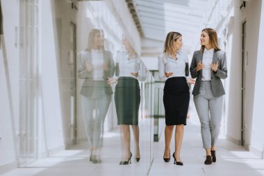 Ofis koridorunda yürüyen ve tartışan iki genç iş kadını.