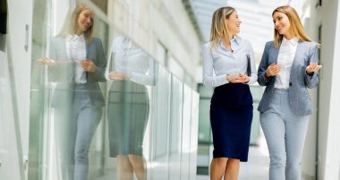 Ofis koridorunda yürüyen ve tartışan iki genç iş kadını.