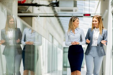 Ofis koridorunda yürüyen ve tartışan iki genç iş kadını.