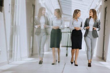 Ofis koridorunda yürüyen ve tartışan iki genç iş kadını.
