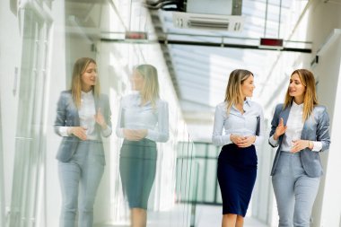Ofis koridorunda yürüyen ve tartışan iki genç iş kadını.