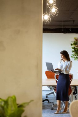 Ofis koridorunda dizüstü bilgisayarı olan güzel bir iş kadını.
