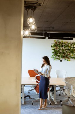 Modern ofiste dijital tabletli genç bir iş kadını duruyor.