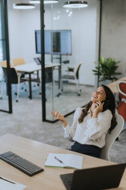 Modern ofiste dizüstü bilgisayarla çalışırken cep telefonu kullanan genç ve güzel bir iş kadını.