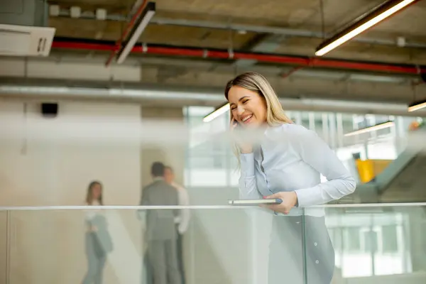 Young business woman with notebook using mobile phone and standing in the modern office wallway