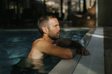 Yakışıklı genç adam, kapalı bir yüzme havuzunun kenarında dinleniyor.