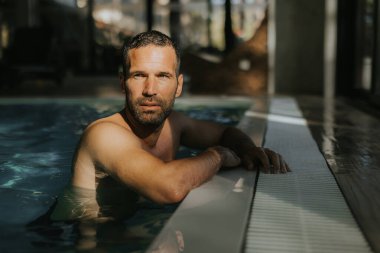Yakışıklı genç adam, kapalı bir yüzme havuzunun kenarında dinleniyor.
