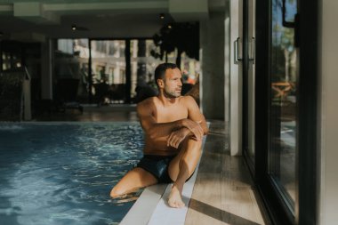 Yakışıklı genç adam, kapalı bir yüzme havuzunun kenarında dinleniyor.