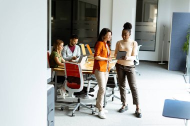 Modern ofiste, takımlarının önünde dijital tabletleri olan iki genç iş kadını.