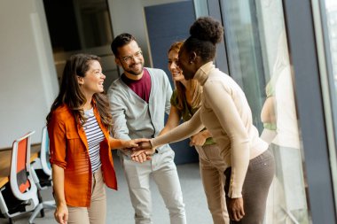 Genç çok ırklı girişim ekibi modern ofiste el ele tutuşuyor.