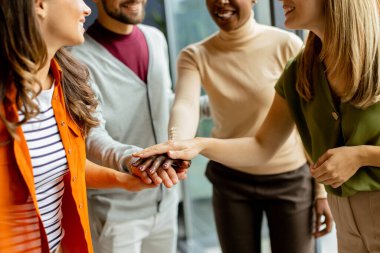 Genç çok ırklı girişim ekibi modern ofiste el ele tutuşuyor.