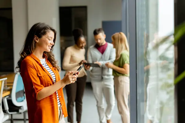 Young business woman woman with mobile phonet in front of her team at the modern office