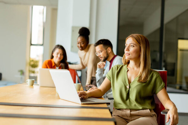 Красивая деловая женщина работает на ноутбуке со своей молодой многонациональной командой стартапов, работающей в современном офисе