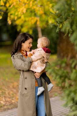 Sonbahar parkında kucağında tatlı bir kız çocuğu tutan genç bir kadın.