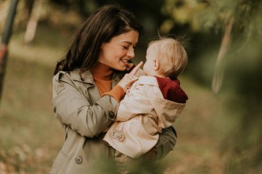 Sonbahar parkında kucağında tatlı bir kız çocuğu tutan genç bir kadın.