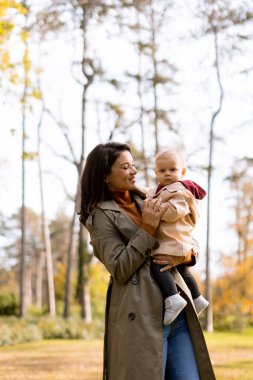 Sonbahar parkında kucağında tatlı bir kız çocuğu tutan genç bir kadın.