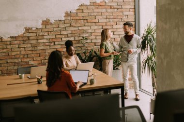 Endüstriyel stil ofisindeki tuğla duvarın yanında çalışan çok ırklı bir grup.