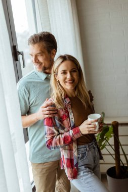 Hafifçe aydınlatılmış bir odada, bir erkek, bir kadına arkadan sarılır. İkisi de pencereden dışarı bakar, birlikte sakin ve samimi bir anı paylaşırlar.