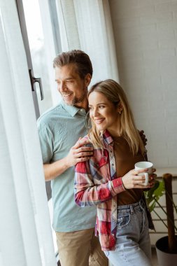 Hafifçe aydınlatılmış bir odada, bir erkek, bir kadına arkadan sarılır. İkisi de pencereden dışarı bakar, birlikte sakin ve samimi bir anı paylaşırlar.