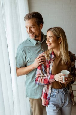 Hafifçe aydınlatılmış bir odada, bir erkek, bir kadına arkadan sarılır. İkisi de pencereden dışarı bakar, birlikte sakin ve samimi bir anı paylaşırlar.