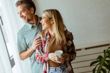 Hafifçe aydınlatılmış bir odada, bir erkek, bir kadına arkadan sarılır. İkisi de pencereden dışarı bakar, birlikte sakin ve samimi bir anı paylaşırlar.