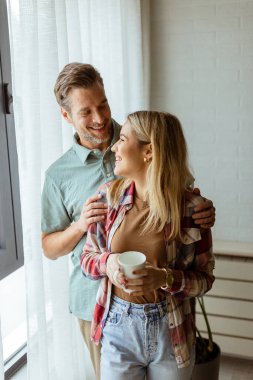 Hafifçe aydınlatılmış bir odada, bir erkek, bir kadına arkadan sarılır. İkisi de pencereden dışarı bakar, birlikte sakin ve samimi bir anı paylaşırlar.