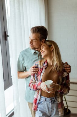 Hafifçe aydınlatılmış bir odada, bir erkek, bir kadına arkadan sarılır. İkisi de pencereden dışarı bakar, birlikte sakin ve samimi bir anı paylaşırlar.