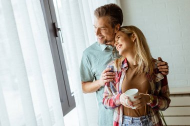 Hafifçe aydınlatılmış bir odada, bir erkek, bir kadına arkadan sarılır. İkisi de pencereden dışarı bakar, birlikte sakin ve samimi bir anı paylaşırlar.