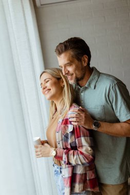 Hafifçe aydınlatılmış bir odada, bir erkek, bir kadına arkadan sarılır. İkisi de pencereden dışarı bakar, birlikte sakin ve samimi bir anı paylaşırlar.