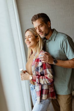 Hafifçe aydınlatılmış bir odada, bir erkek, bir kadına arkadan sarılır. İkisi de pencereden dışarı bakar, birlikte sakin ve samimi bir anı paylaşırlar.