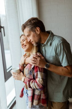 Hafifçe aydınlatılmış bir odada, bir erkek, bir kadına arkadan sarılır. İkisi de pencereden dışarı bakar, birlikte sakin ve samimi bir anı paylaşırlar.