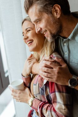 Hafifçe aydınlatılmış bir odada, bir erkek, bir kadına arkadan sarılır. İkisi de pencereden dışarı bakar, birlikte sakin ve samimi bir anı paylaşırlar.